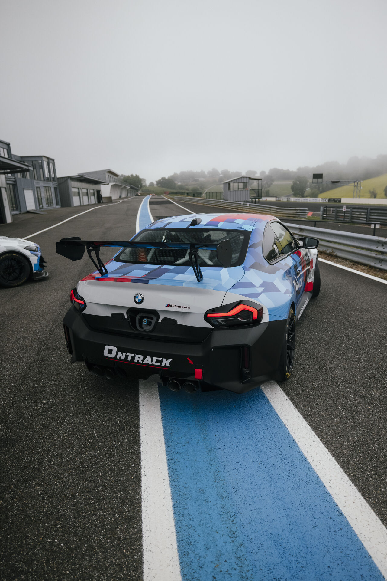 BMW M2 Racing ONTRACK vue arrière sur la ligne droite du circuit dans la brume