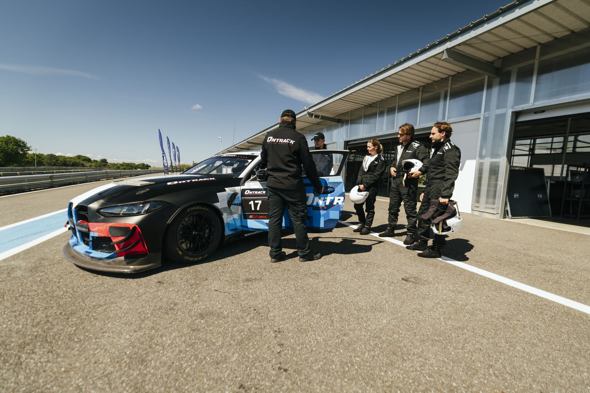 Équipe ONTRACK et pilotes en combinaison devant une BMW M4 GT4 sur circuit